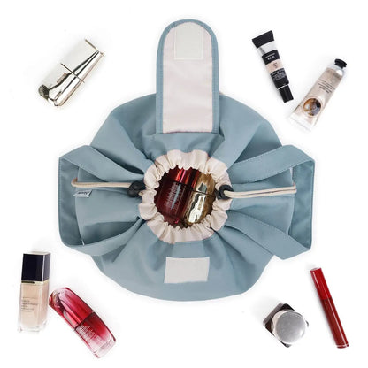 Grey-blue drawstring makeup bag opened flat to show its gathered closure and handles