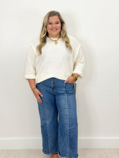 Off-white knit top with 3/4 folded sleeves and round neckline, ribbed pattern