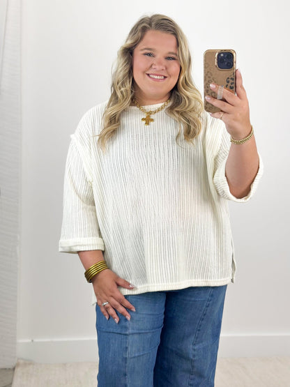 Off-white knit top with 3/4 folded sleeves and round neckline, ribbed texture